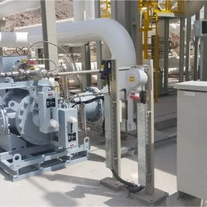 Industrial facility with large pipes, valves, and mechanical equipment, including a pump system and measurement devices, situated outdoors in a structured metal framework