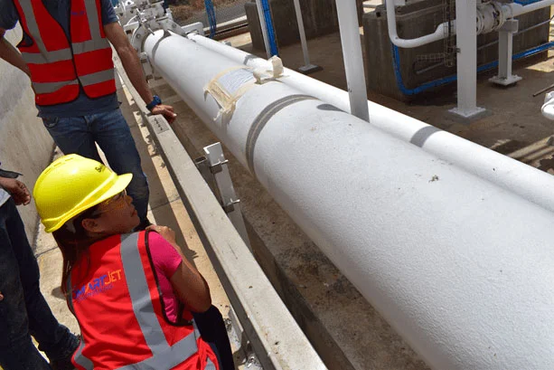 Technicians wearing safety vests and helmets inspecting an industrial pipeline on site